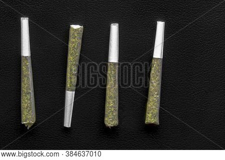 Four Pre-roll Cannabis Joints On A Black Leather Surface