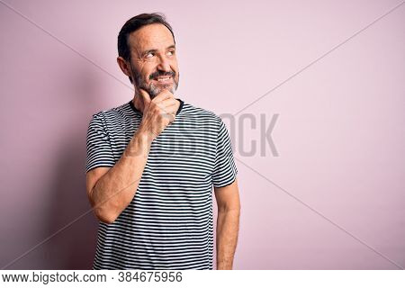 Middle age hoary man wearing casual striped t-shirt standing over isolated pink background with hand on chin thinking about question, pensive expression. Smiling with thoughtful face. Doubt concept.