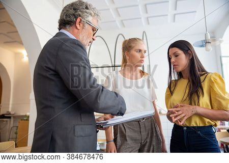 Mature Loan Inspector With Notepad Visiting Young Entrepreneurs Onsite. Business People In Office In