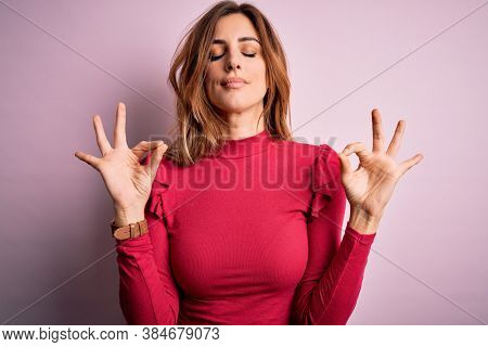 Young beautiful brunette woman wearing casual sweater stnding over pink background relax and smiling with eyes closed doing meditation gesture with fingers. Yoga concept.