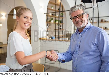 Happy Business Partners Of Different Ages Meeting And Shaking Hands. Mature Man And Young Woman In C
