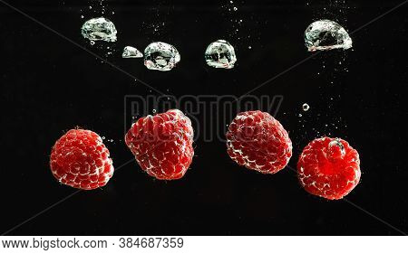 Raspberries Splashing Into Clear Water Isolated On Black Background. Healthy Fruits Concept. Copy Sp