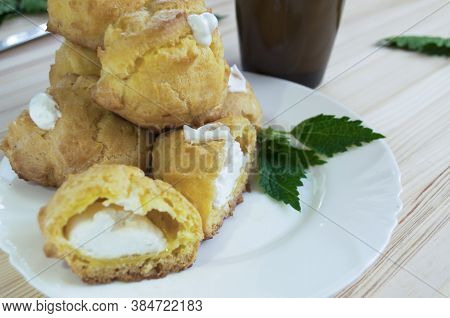 Portion Of Eclairs Filled With Whipped Cream With A Cup Of  Coffee With Milk On A Wooden Background.