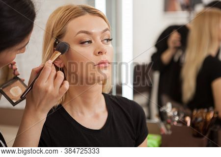 Makeup Artist Applying Highlighter On Cheekbones Of A Gorgeous Blonde Woman