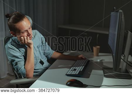Tired Young Man Sitting In Front Of His Computer Late At Night. Male Freelancer Working At Night. Pr