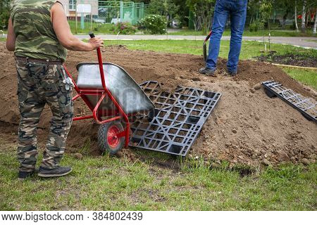 The Gardener Sprinkles A Flower Bed With A Shovel. Creation Of Landscape Design In The Garden. The M