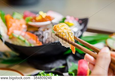 Hand Holding Wooden Chopsticks Tongs Sushi At Japanese Food Restaurant.