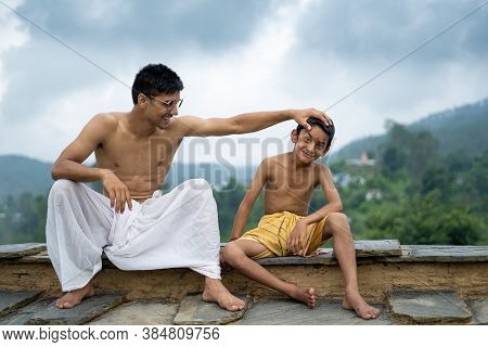 A Young Man Sitting On The Roof With His Younger Brother,both Wearing Dhoti, Smiling Into The Camera