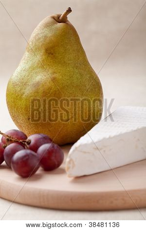 Zelená hruška, sýr Brie, červené hrozny na dřevěném prkénku makro
