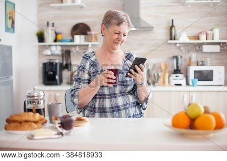 Leisure Morning For Senior Woman Using Modern Technology In Bright Cozy Kitchen. Authentic Elderly P