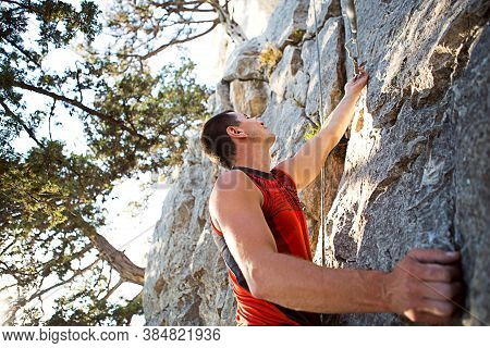 Climber In Red T-shirt Climbs A Gray Rock. A Strong Hand Grabbed The Lead, Selective Focus. Strength