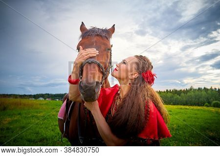 A Woman In A Bright Gypsy Dress And Image With A Horse In A Field With Green Grass. A Model Or Actre