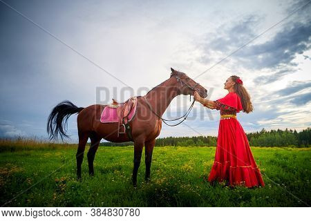 A Woman In A Bright Gypsy Dress And Image With A Horse In A Field With Green Grass. A Model Or Actre