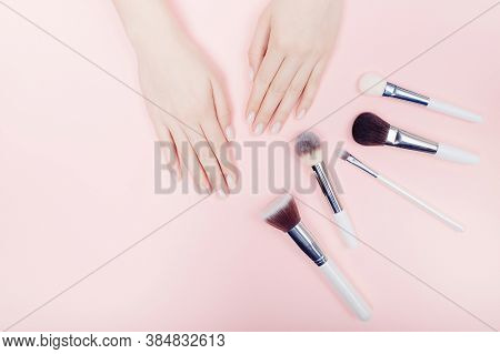 Female Hand With Makeup Brushes On Pink Color Background. Top View Point, Flat Lay