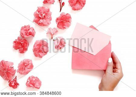 Hand Keeps Pink Envelope Near Pink Flowers  Over A White Background Top View