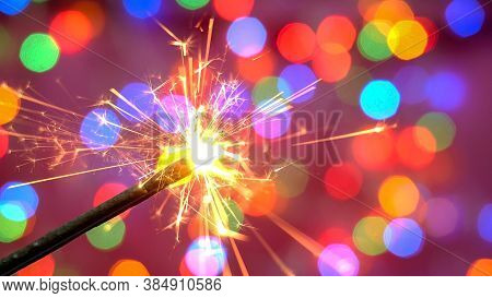 Bright Burning Sparkler Against The Backdrop Of Defocused Multicolored Garland. Blurred Backdrop. Me