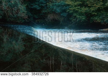 Small Waterfall On The Clyde River. The Mirrored Surface Of The River Reflects A Dense Forest On The