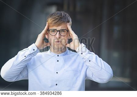 Portrait Of A Shock, Handsome European Guy, Holding His Head With Both Hands, Formally Dressed In A 