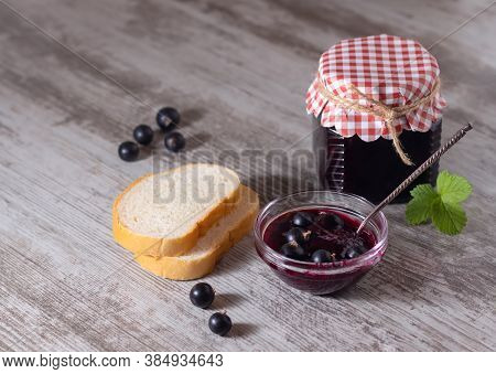 Jar Of Delicious Homemade Blackcurrant Jam, Slices Of Bread And Fresh Berries On A Gray Wood Backgro