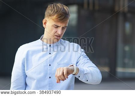 Portrait Of An Upset, Handsome European Guy, Looking At His Watch On His Hand, Formally Dressed In A