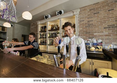 Portrait of confident bartender at counter with coworkers in background