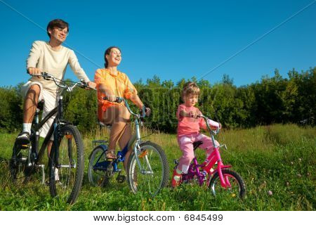 Far, mor og datter gå til drev solskinsdag på cykler