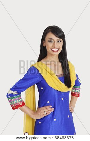 Portrait of beautiful Indian woman in traditional wear standing with hands on hips over gray background