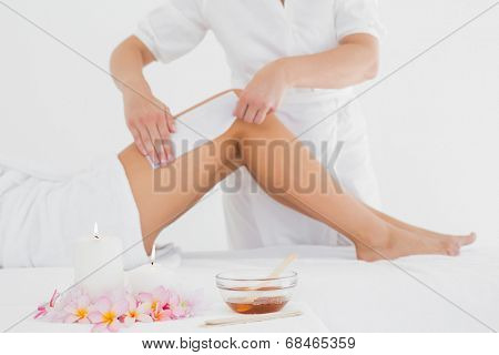 Mid section of therapist waxing woman's leg at spa center