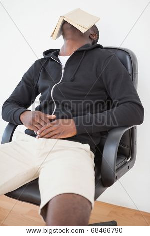 Casual man sitting on swivel chair with book over face at home in the living room
