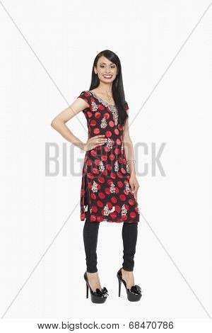 Full length portrait of Indian female in traditional wear standing with hand on hip over gray background