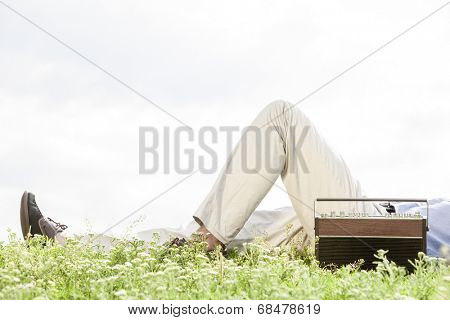 Low section of man lying by vintage radio on grass against clear sky