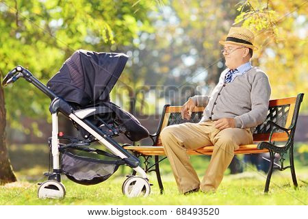Grandfather sitting and looking at his baby nephew in a stroller, in a park