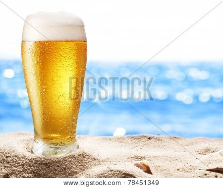 Photo of cold beer botle in the sand. Sparkling sea at the background.