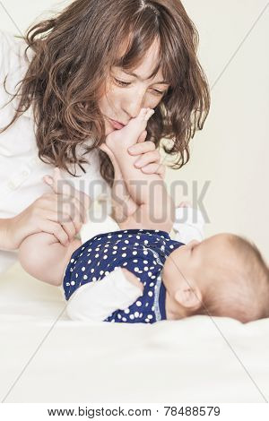 Young And Happy Mother Having Good Time Together With Her Baby Infant By Kissing Her Little Legs