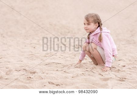 little girl kneeling on the sand and looking ahead