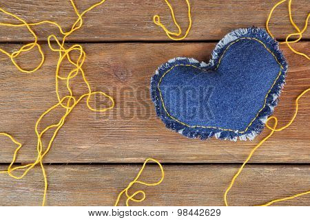 Denim heart and thread on wooden background