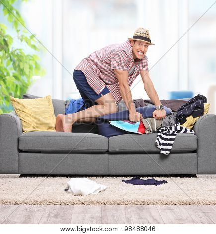 Young guy packing clothes into a briefcase on a gray sofa at home shot with tilt and shift lens