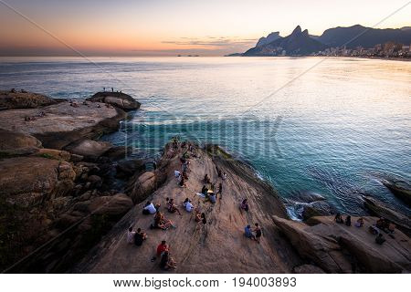 Rio de Janeiro, Brazil - June 30, 2017: People sitting all around on Arpoador rock and enjoying beautiful sunset.