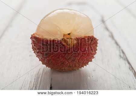 half peeled lichee on white wood background