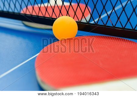 pingpong rackets and ball and net on a blue pingpong table close up
