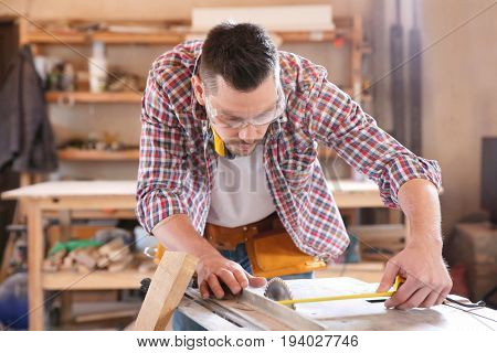 Carpenter taking measurements for working with wooden plank in shop
