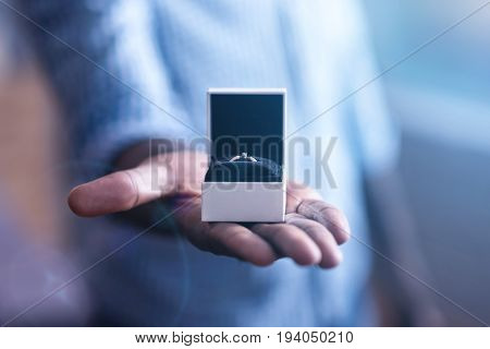Our engagement ring. Pleasant young inspired African American manstanding in the studio and holding the engagement ringwhile expressing happiness