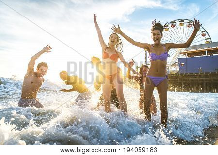 Group of friends splashing water while swimming in the sea - Multi-ethic group of people having fun on the beach
