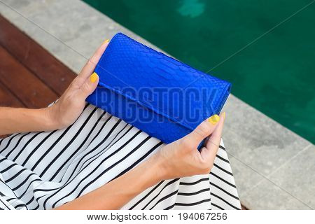 Luxury fashion snakeskin python wallet in woman hands outdoors, shoot near the swimming pool.