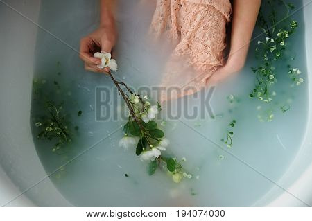 Beautiful romantic red-haired girl sitting in the bath and holding flowers .The face is not visible. In lace dress powdery pastel cream color