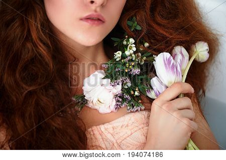 Beautiful romantic red-haired girl sitting in the bath and holding flowers .part of the face is not visible. In lace dress powdery pastel cream color