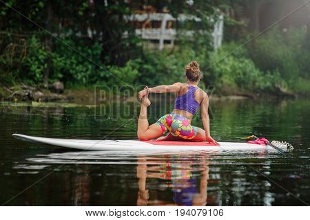 Young Woman Doing Fitness On A Board With An Oar. Side View - The Concept Of Harmony With Nature, A