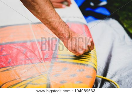 Close up view of hand waxing surf board outdoors. Man is removing or applying wax to surfboard shortboard on vacation. Traces of wax are visable.