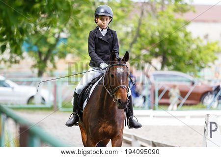 Young teenage girl in helmet riding horse on dressage equestrian competition