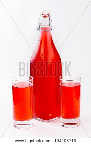 Berry red drink in a glass bottle, poured into two glasses on a white background